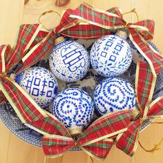 four blue and white ornaments in a bowl on a wooden table with ribbon around them