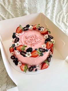 a birthday cake decorated with strawberries and blackberries in a box on a table