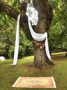 a tree with white drapes hanging from it's branches and flowers on the ground