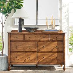 a wooden dresser with two mirrors above it and a potted plant next to it