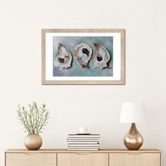 three seashells framed in wooden frame on wall next to table with lamp and vase