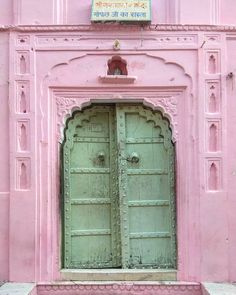 an old pink building with two green doors in the middle and a sign above it