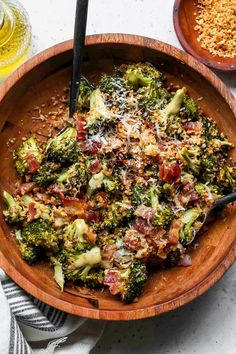 a wooden bowl filled with broccoli covered in cheese and other toppings next to a glass of beer