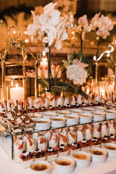 a table topped with lots of desserts and flowers on top of each other in front of candles