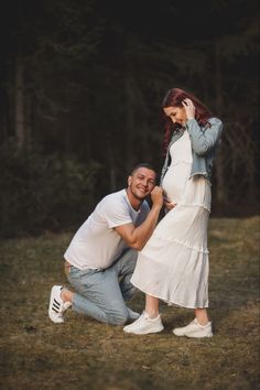 a man kneeling down next to a woman in a white dress while she holds her hand on her head