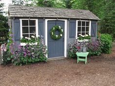 a garden shed with flowers around it and a bench in the yard next to it