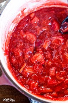 a large pot filled with red sauce on top of a wooden table