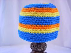 a crocheted hat is on top of a wooden headdress with an orange, blue and yellow stripe