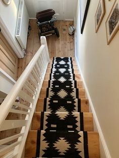 a black and white rug on the bottom of a stair case next to a wooden handrail