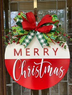 a merry christmas sign hanging on the front door of a house with red and green bows