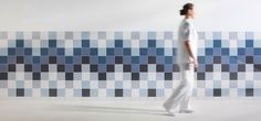 a woman standing in front of a blue and white tiled wall with squares on it