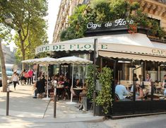 people are sitting at tables in front of a cafe on the side of the street