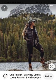 a woman standing on top of a rock next to a lake with trees in the background