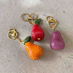 three key chains with fruits on them sitting on the ground next to eachother