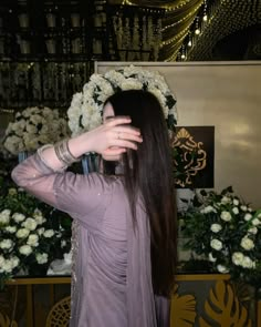 a woman with long hair standing in front of flowers and holding her hand up to her face