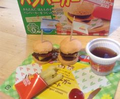 two hamburgers with pickles and ketchup on a table next to a box of japanese fries