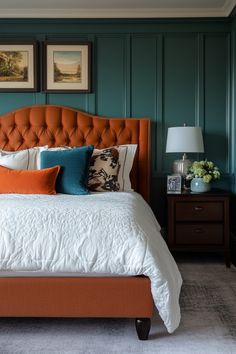 a bed with orange and blue pillows in a bedroom next to two pictures on the wall