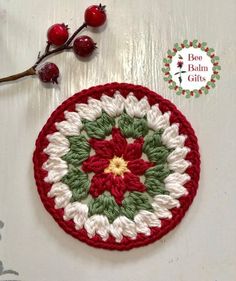 a crocheted christmas ornament with red and green flowers on it next to a branch