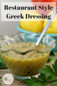 a glass bowl filled with greek dressing next to lemons and parsley