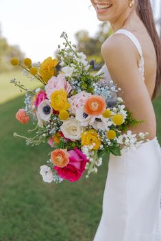 a woman in a white dress holding a bouquet of flowers and smiling at the camera