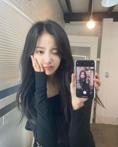 a woman taking a selfie with her cell phone in front of her face and wearing a black top