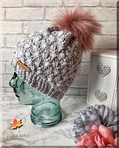 a crocheted hat with a pink pom - pom on it next to some flowers