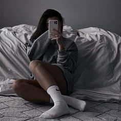 a woman sitting on top of a bed while holding a cell phone in her hand