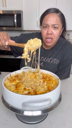 a woman holding a wooden spoon full of macaroni and cheese in a white casserole dish