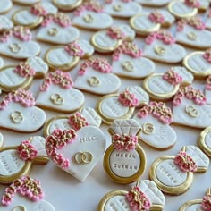 many decorated cookies are arranged on a table with pink and gold bows, hearts, and wedding rings