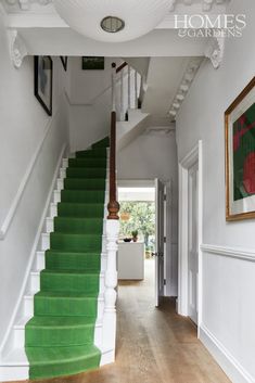 a green carpeted staircase leading up to a white wall with framed pictures on it