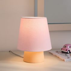 a pink car is sitting on the table next to a book and a small lamp