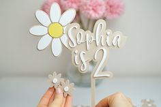 a person holding a cake topper in front of a vase with flowers on it