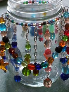 a glass jar filled with lots of different colored beads and chains hanging from it's sides