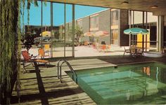 an indoor swimming pool with chairs and umbrellas in front of large windowed windows