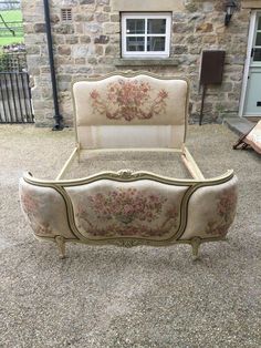 an antique bed frame with flowers on it in front of a stone wall and door