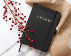 a black journal with red berries on it next to a burlock and ribbon