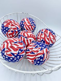 six red, white and blue decorated balls in a wire basket with american flags on them