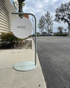 a sign that says hesed on it next to a sidewalk with trees in the background