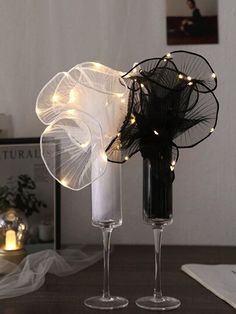 two wine glasses with lights on them sitting on a table next to a vase filled with flowers