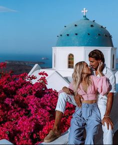 a man and woman sitting next to each other in front of a building with pink flowers