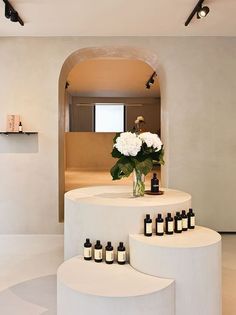 a white counter with bottles and flowers on it in a room that has an archway leading to the bathroom