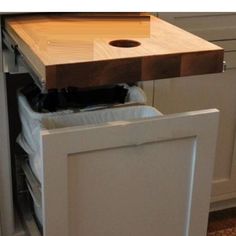 a kitchen cabinet with a cutting board on top of it and trash in the bottom drawer