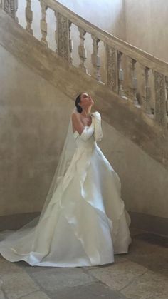 a woman in a white wedding dress standing next to a stair case and looking up at the sky