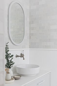 a white sink sitting under a bathroom mirror next to a vase filled with green plants