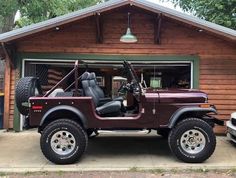 a jeep parked in front of a garage with an open door and two large tires