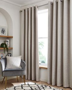 a living room filled with furniture and a large window covered in grey drapes next to a white rug