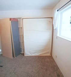 an empty room with a refrigerator and other items in the corner, next to a window