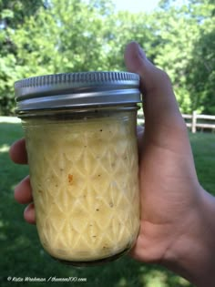 a hand holding a mason jar filled with food in the middle of a grassy area