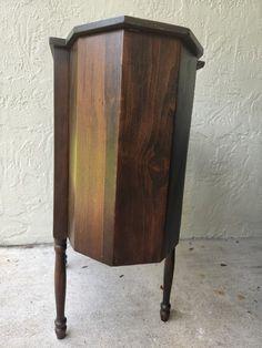 a small wooden cabinet sitting on top of a cement floor next to a white wall