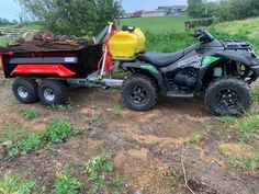 an atv pulling a trailer full of wood on the side of a dirt road in front of a field